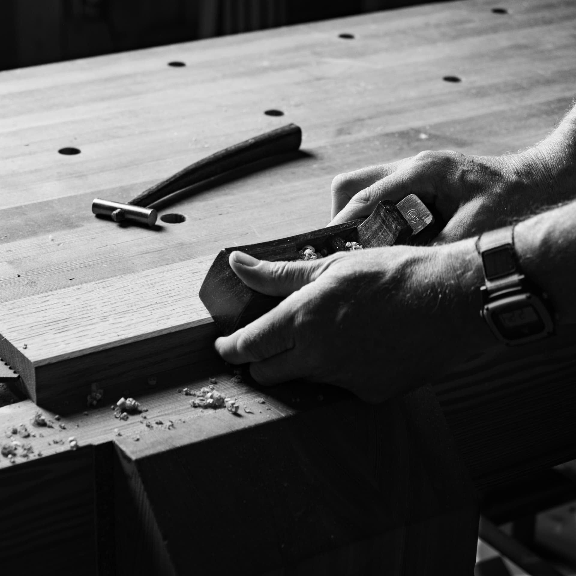 Laël Gordon pushing a wooden hand plane across a plank at the workbench
